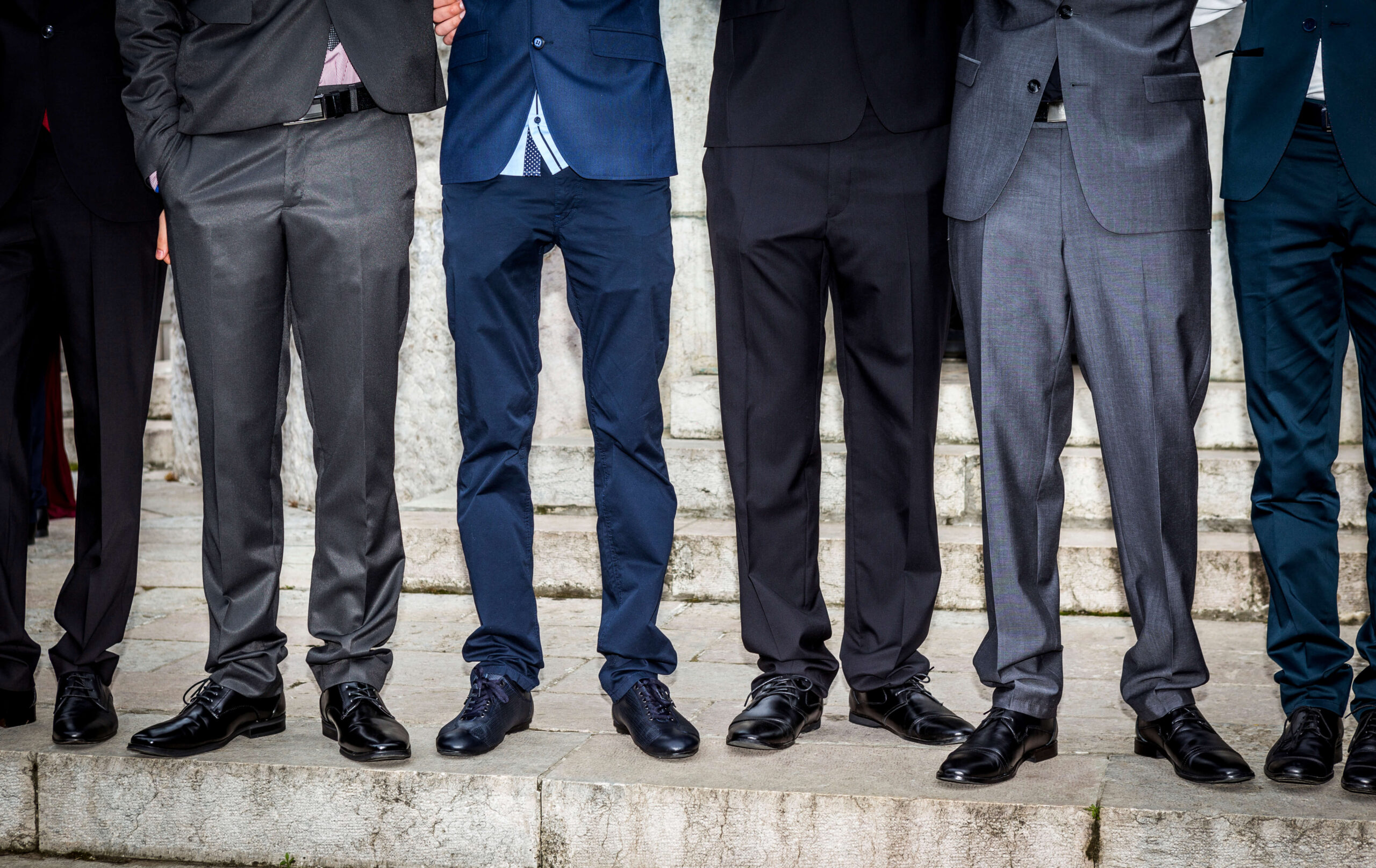Six pairs of men wearing suits; image of legs standing in horizontal line.