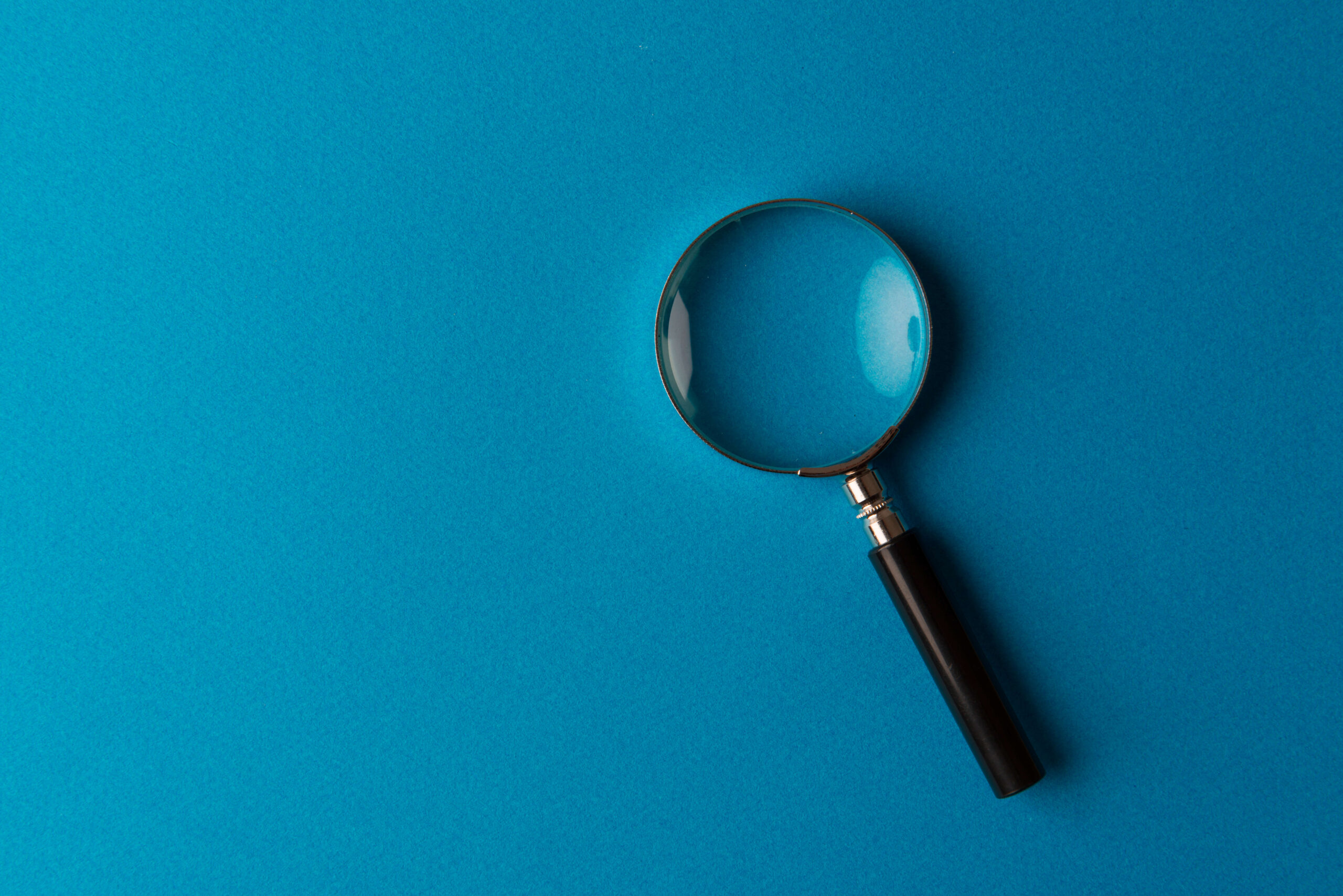 Magnifying glass against teal background.