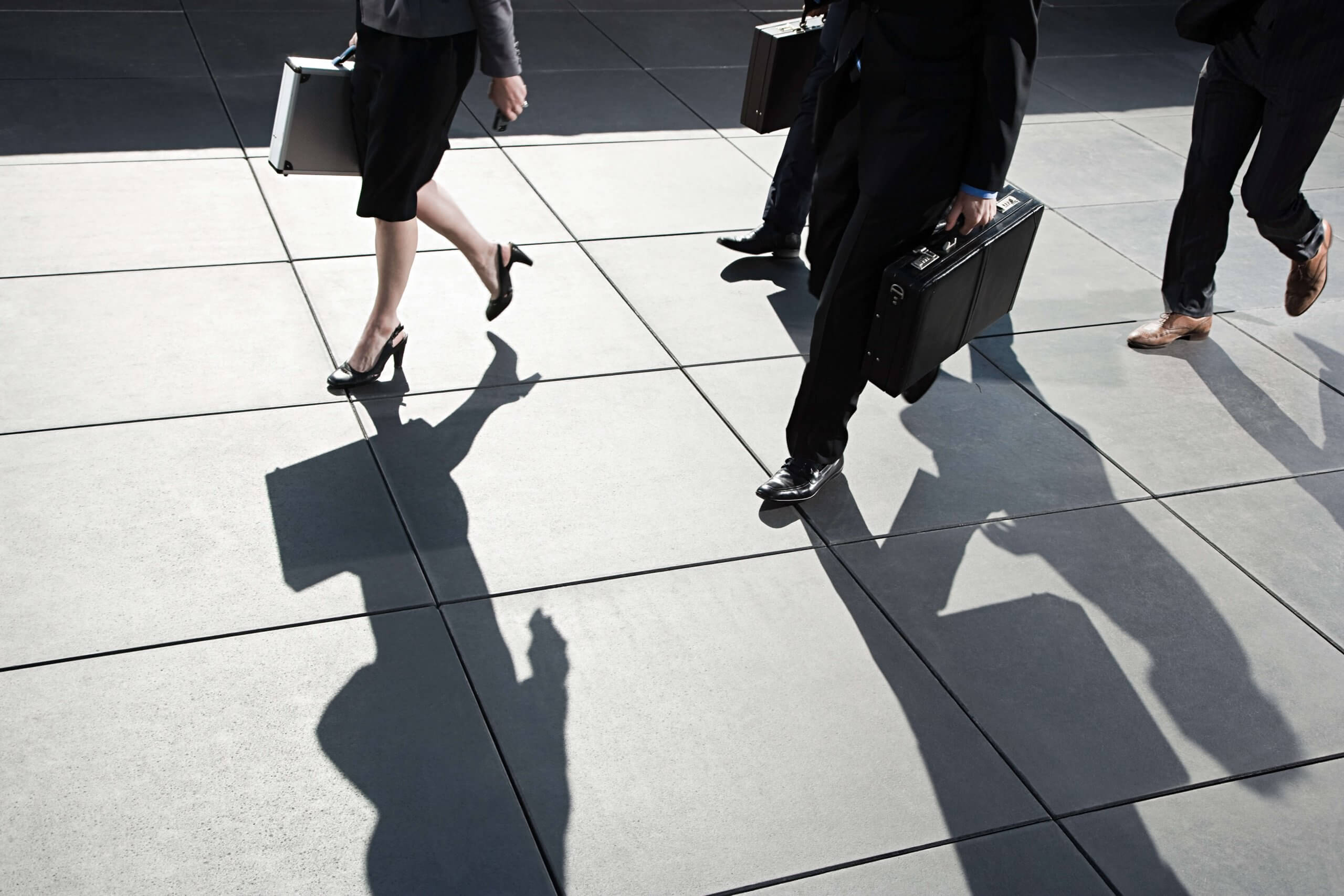 four businesspeople with suitcases walking across a concrete plaza