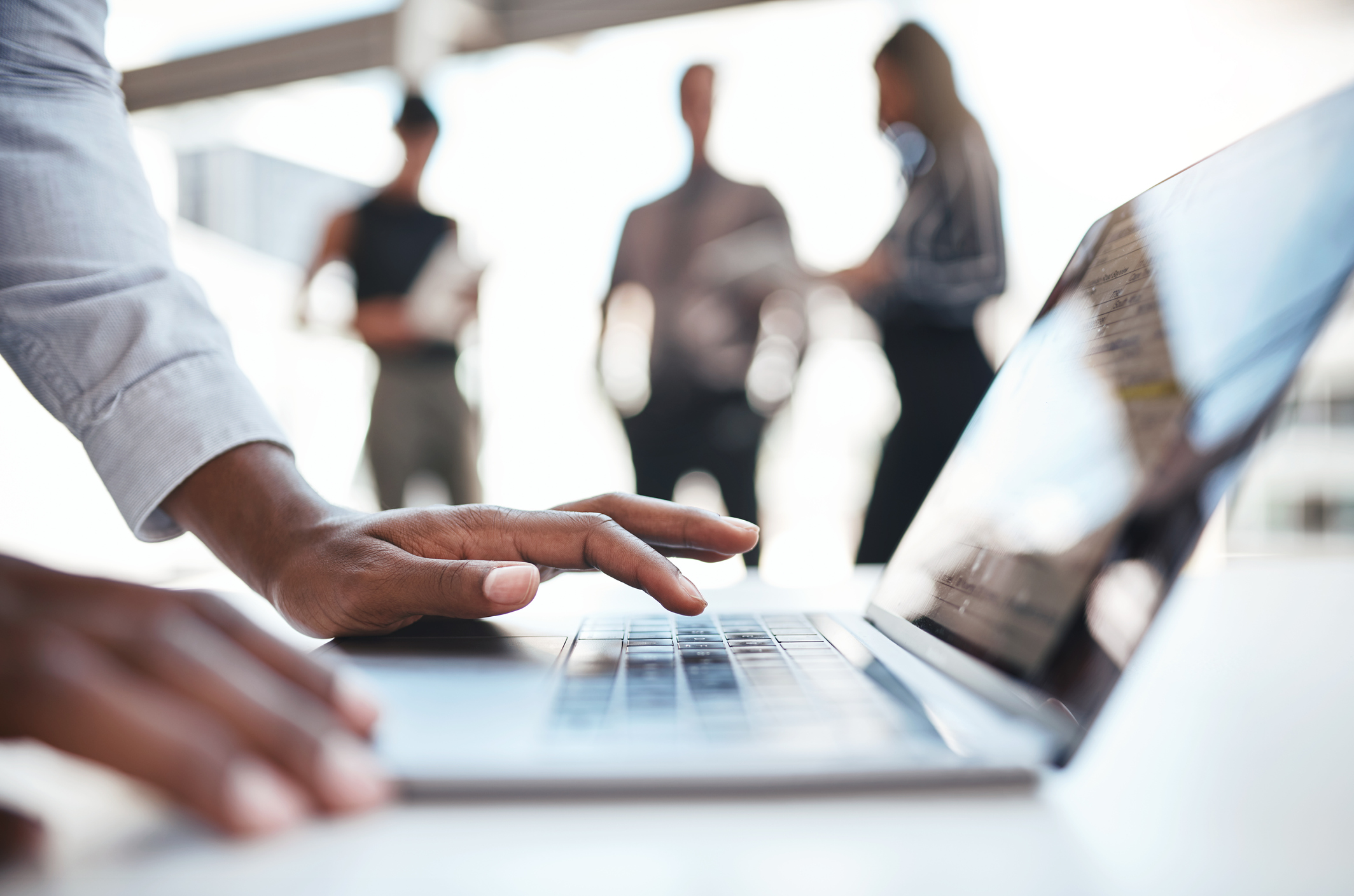 Cropped shot of an unrecognizable businessman using a laptop while his colleagues stand in the background