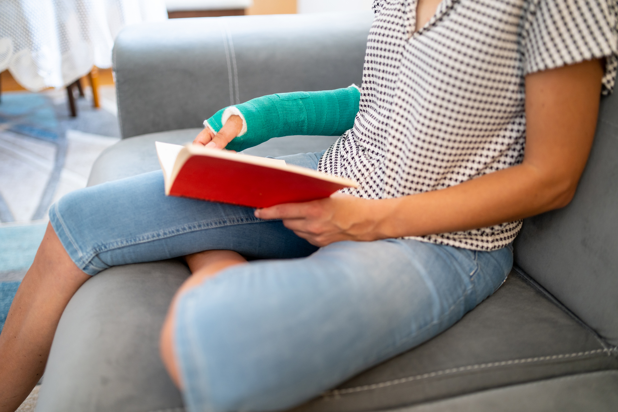 Woman with broken arm reading a book at home