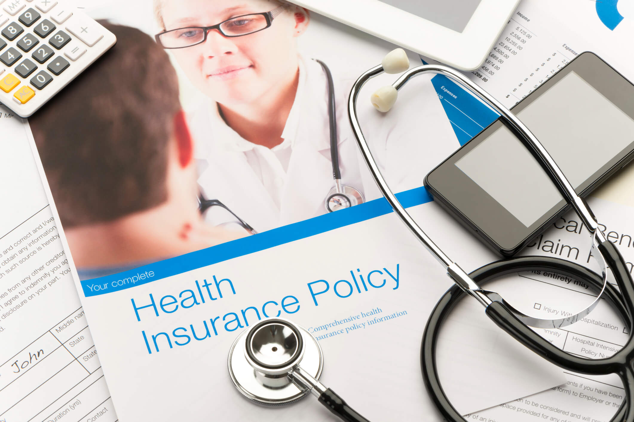 Health Insurance Policy brochure with paperwork, a stethoscope, mobile phone and digital tablet