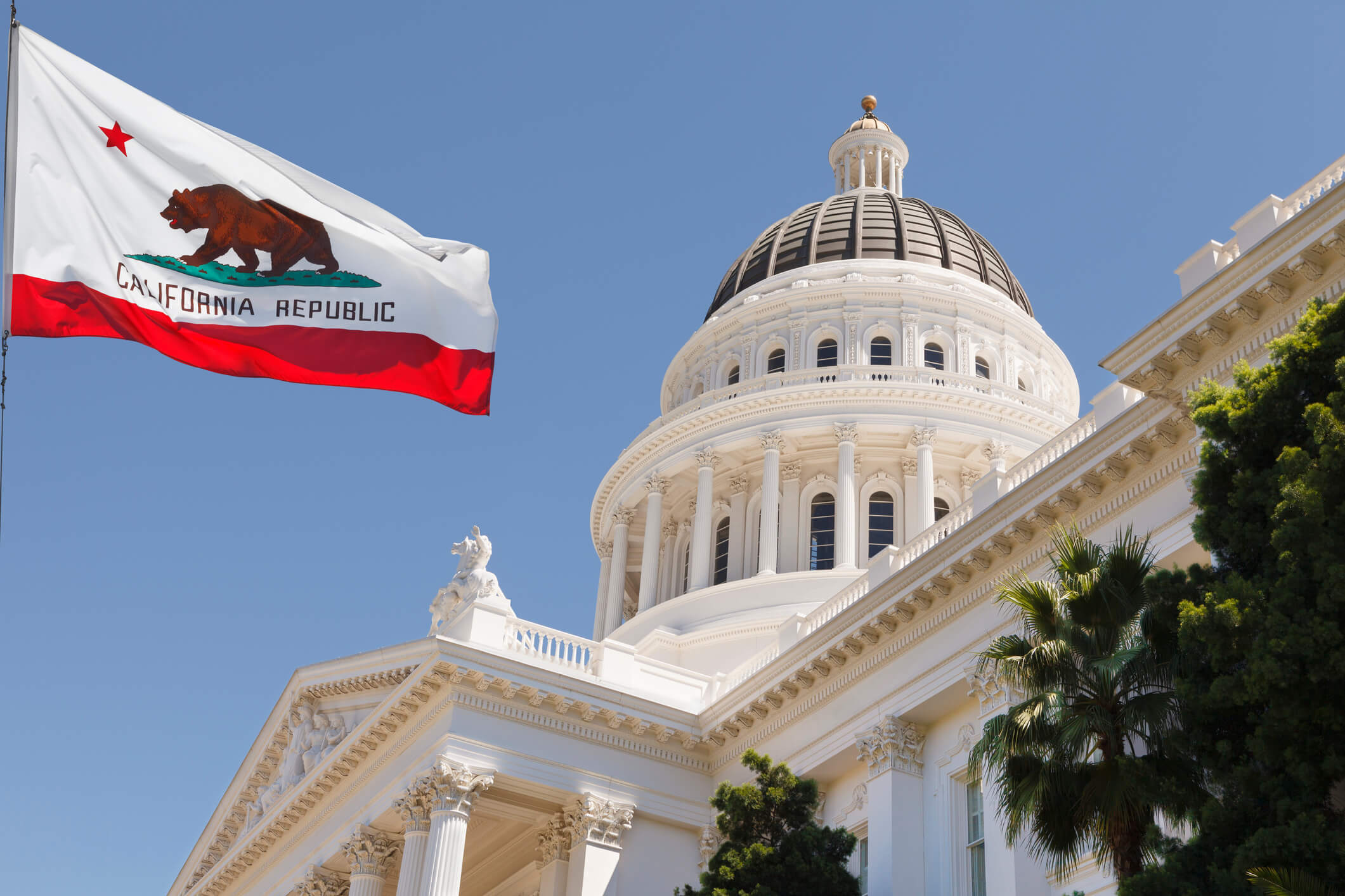 California State Capitol building with state flag in Sacramento on a windy summer day with clear sky