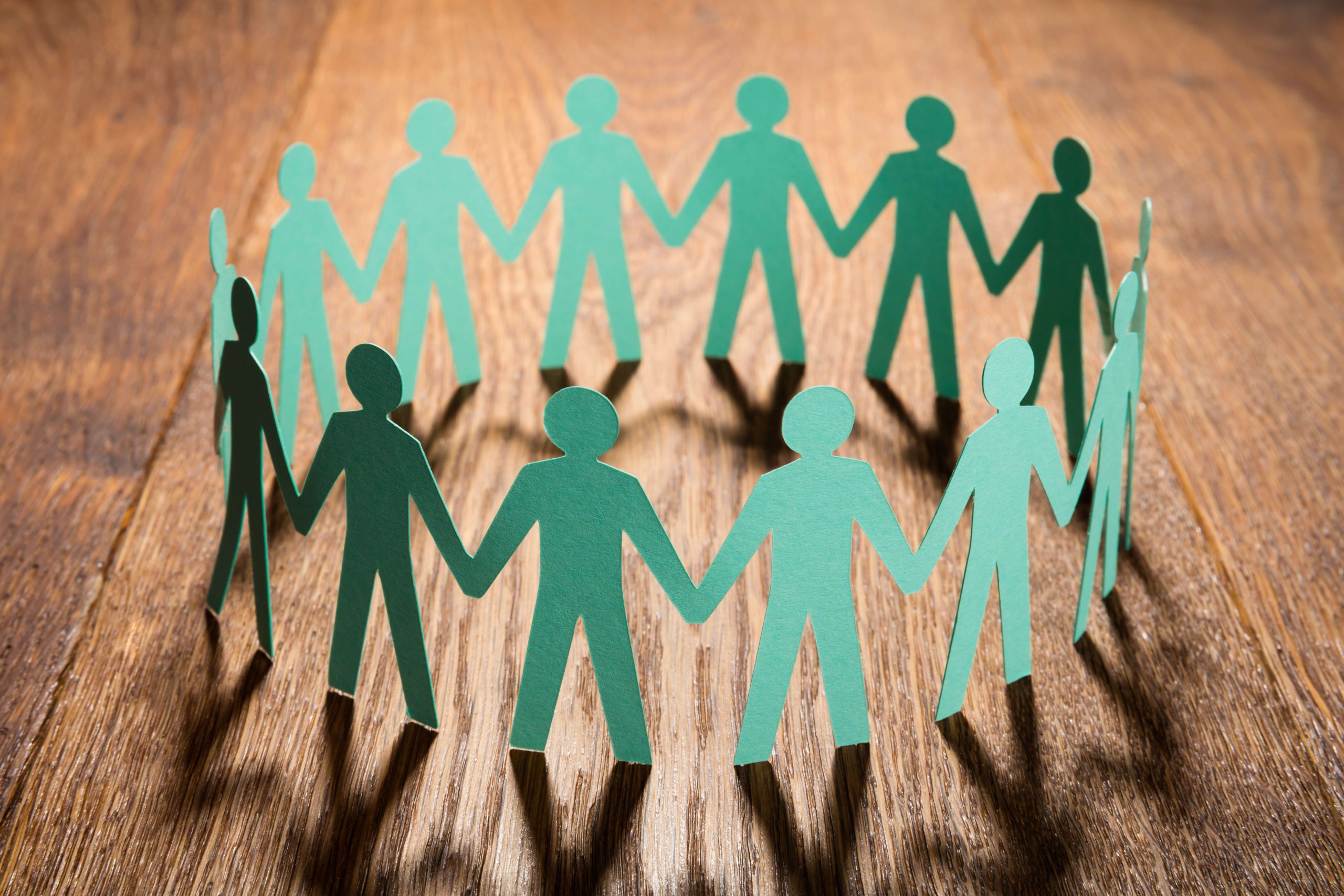 circle of simple green paper dolls on wooden table