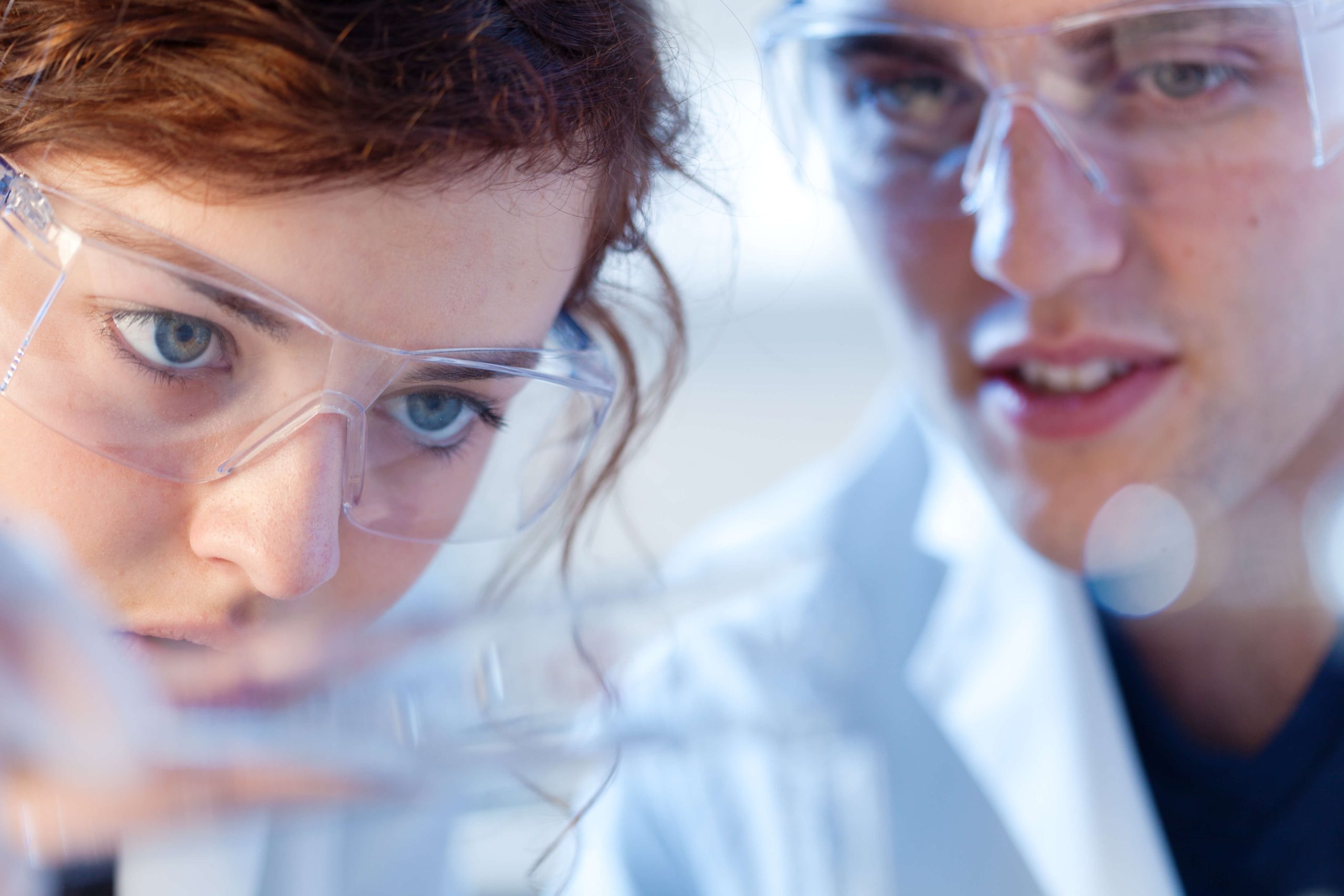 two laboratory technicians working together with safety glasses on, close on faces